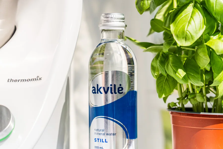 Akvilė still mineral water bottle beside fresh green leaves