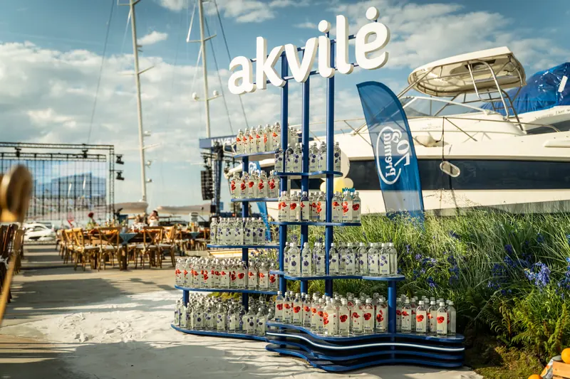An Akvilė display beside boats and outdoor tables at a marina