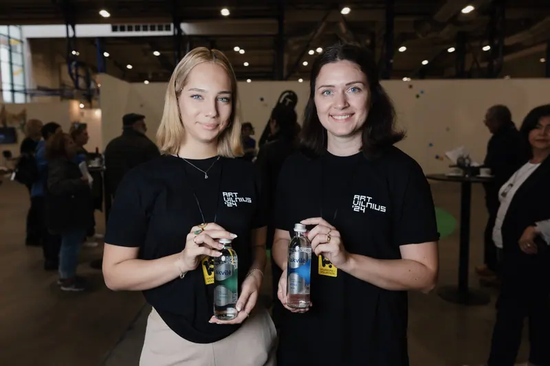 Two guests holding Akvilė bottles at an indoor cultural gathering