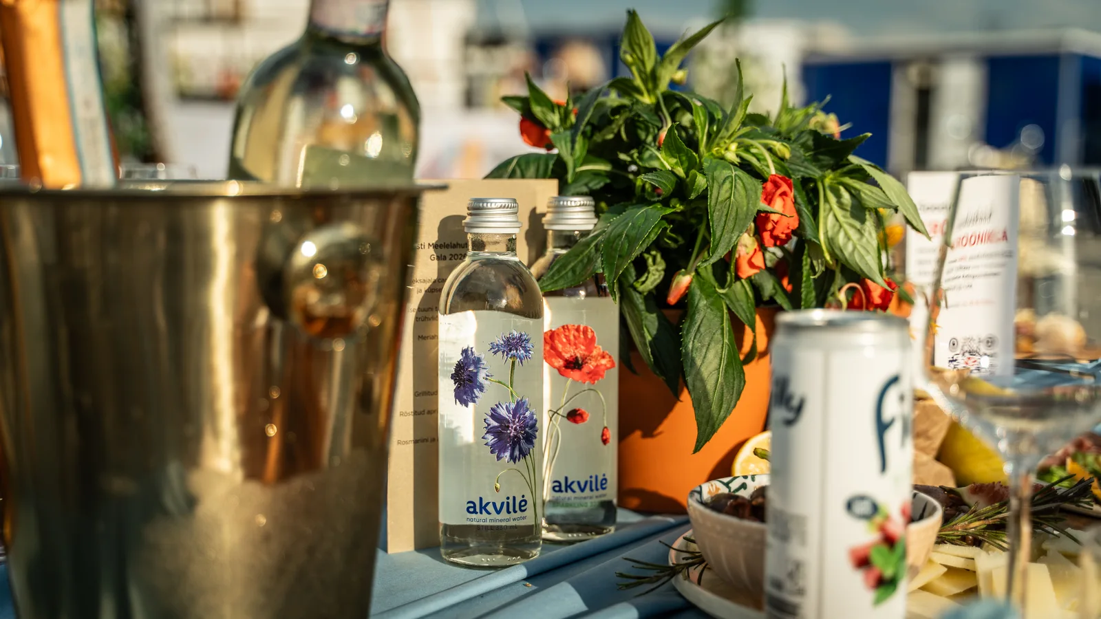 Akvilė floral bottles among glasses, flowers and place settings at a waterfront table