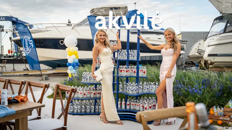 Guests standing beside Akvilė bottles and boats at an outdoor event