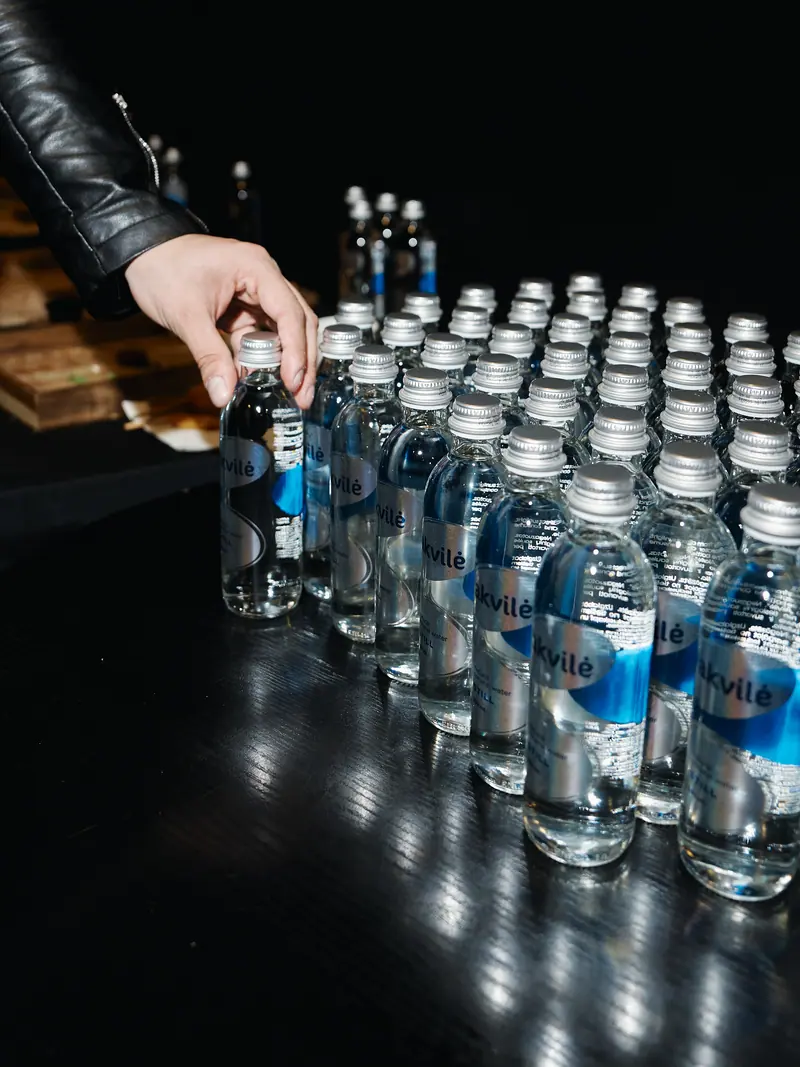 A guest reaching for a floral Akvilė glass bottle at a reception