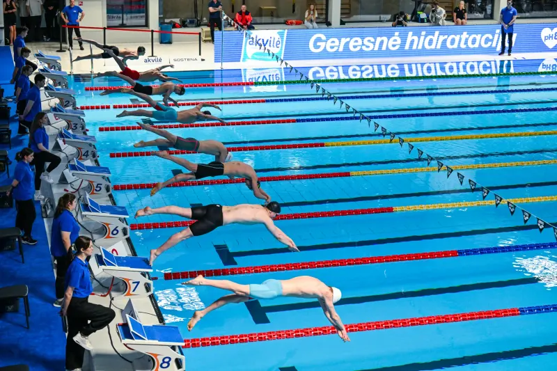 Swimmers racing at a competition with Akvilė branding beside the pool